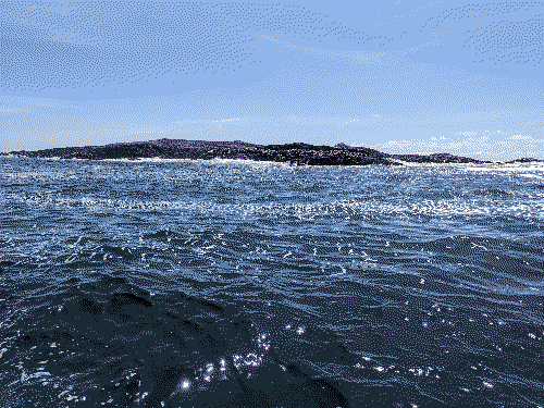 Deep blue sea with white seam foam surrounds a small outcrop on a bright and sunny day.