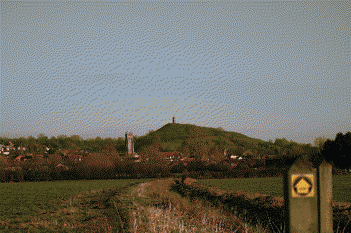 Glastonbury tor sits atop it's hill in the centre of the image. An untrodden path goes towards it.