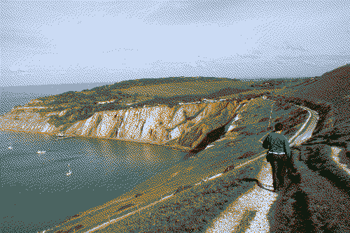 A coastal path with cliffs off to the left, and a few yachts float in the sea.