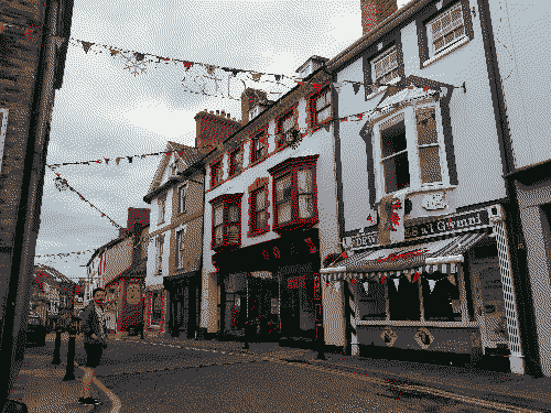 A welsh street with red and white bunting between the buildings. A welsh flag hangs from a window on the first floor.